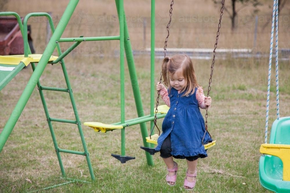 Little girl playing on a swing set and slide in the backyard - Australian Stock Image
