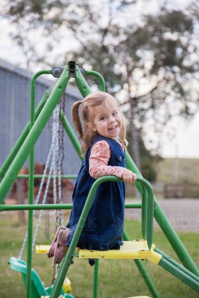 Little girl playing on a swing set and slide in the backyard - Australian Stock Image