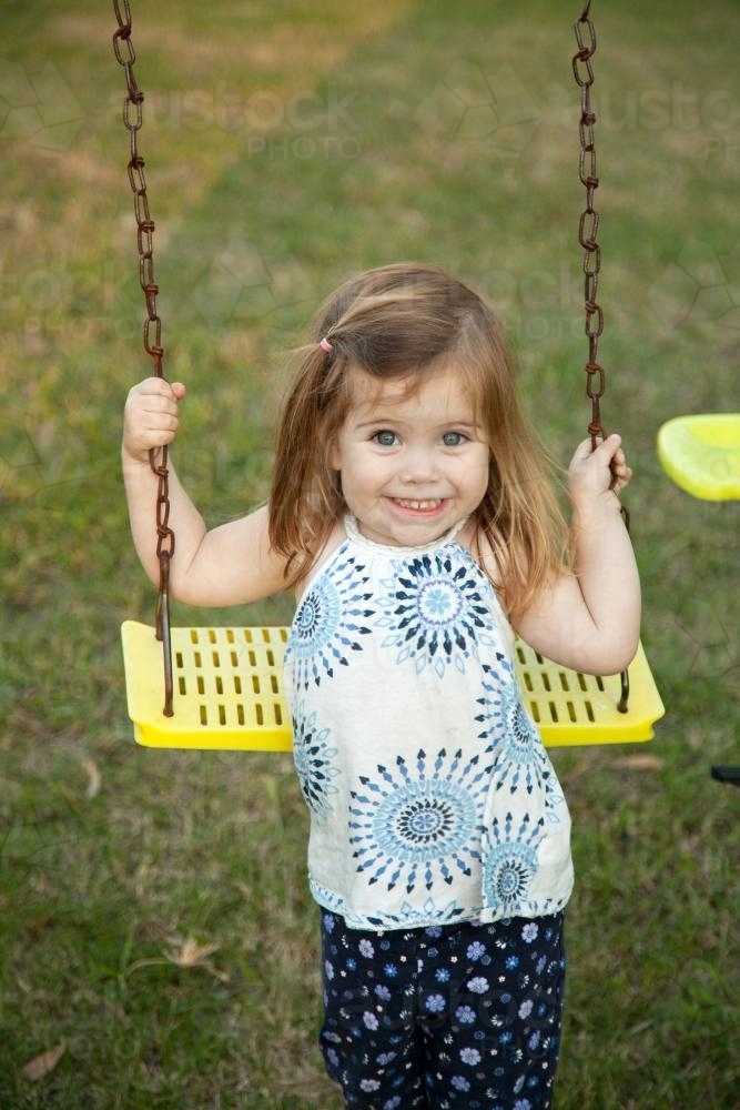 Little girl playing on the swings in the backyard - Australian Stock Image