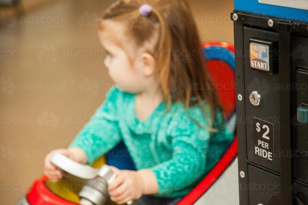 Little girl playing on two dollar kiddie ride at the supermarket - Australian Stock Image