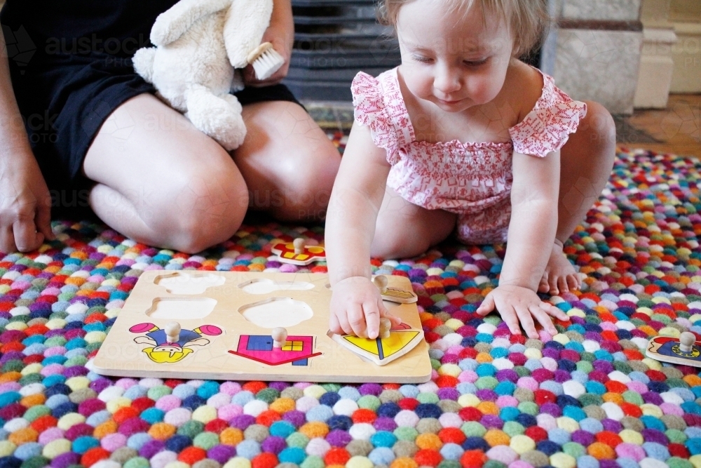 Little girl playing with a puzzle on a rug - Australian Stock Image