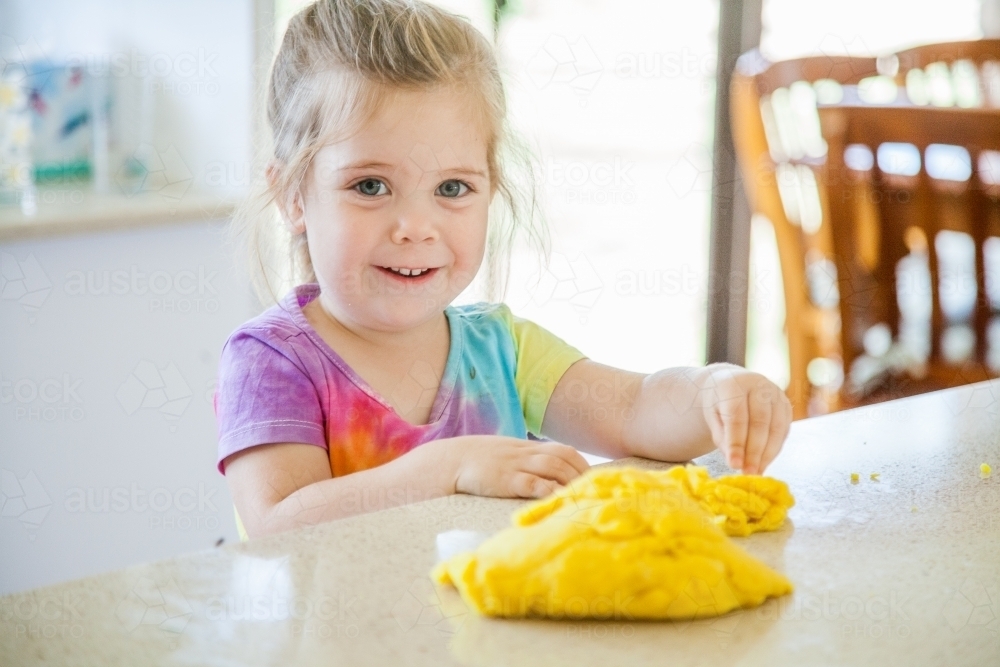 Little girl playing with yellow playdough at home - Australian Stock Image