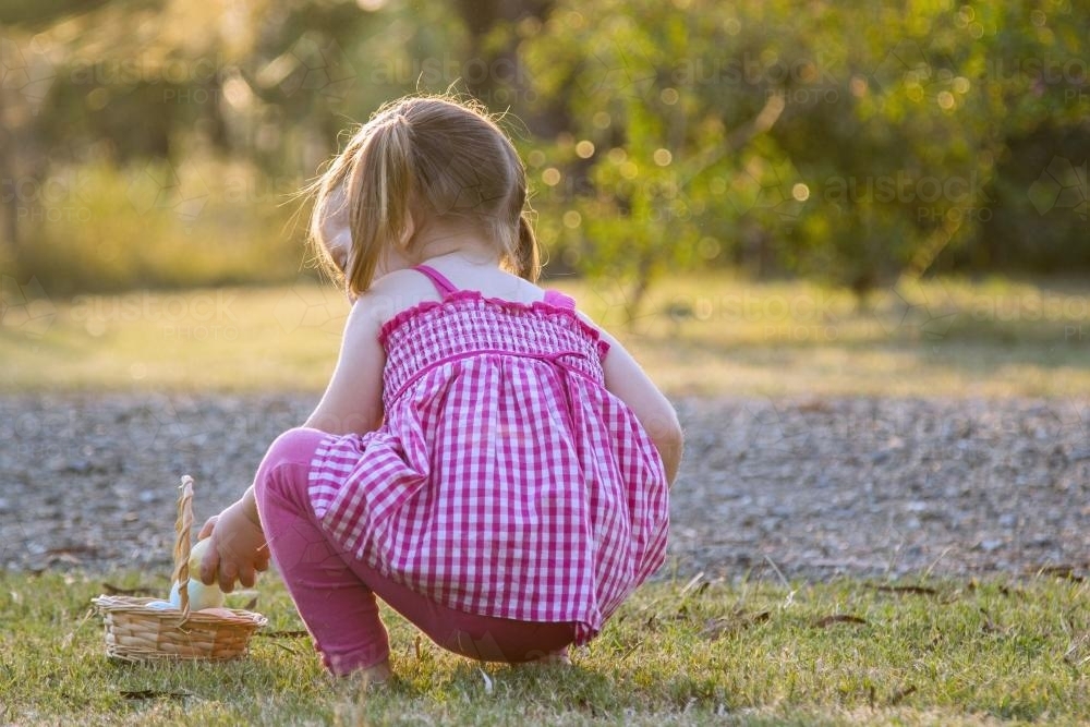 Little girl putting Easter eggs in a basket - Australian Stock Image