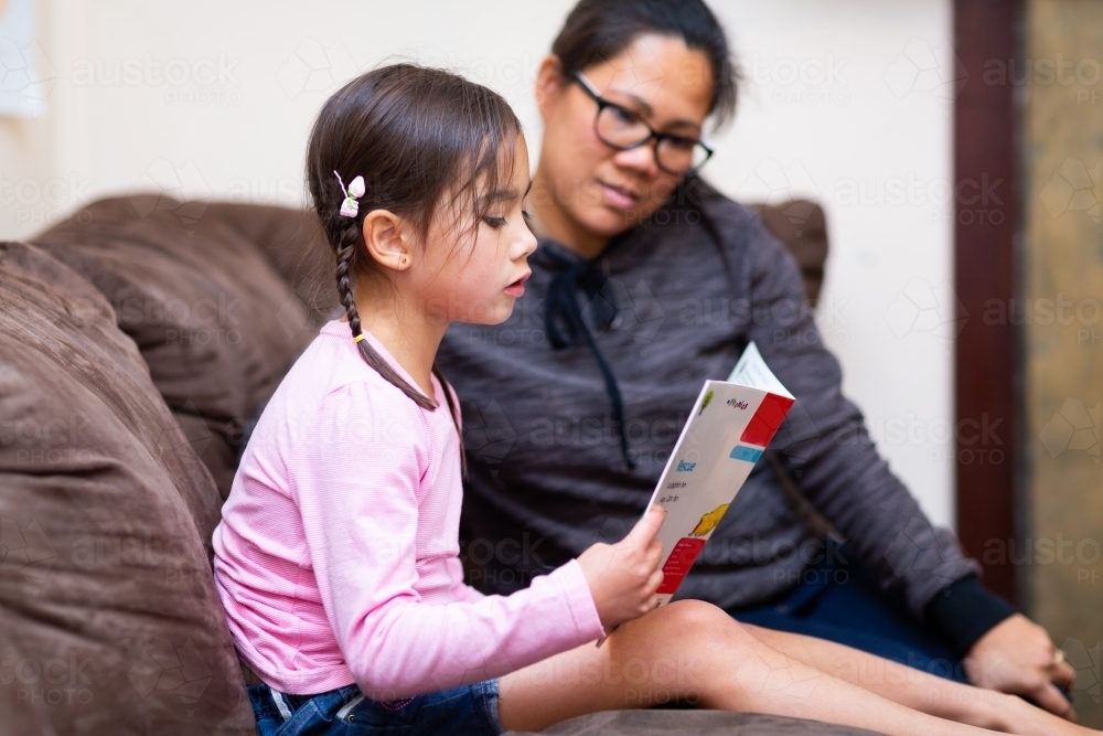 Little girl reading book with mother - Australian Stock Image
