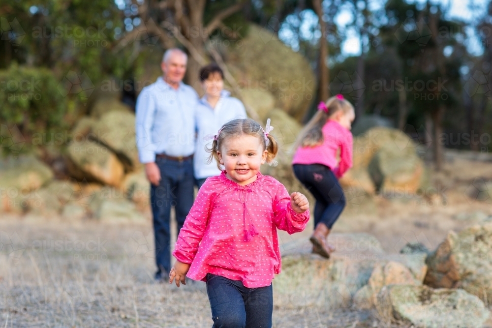 Little girl running towards camera with family in background - Australian Stock Image