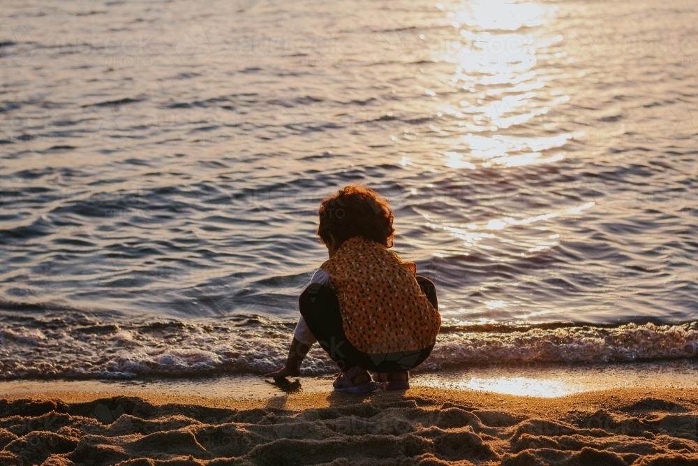 Little girl silhouette at the beach touching water - Australian Stock Image