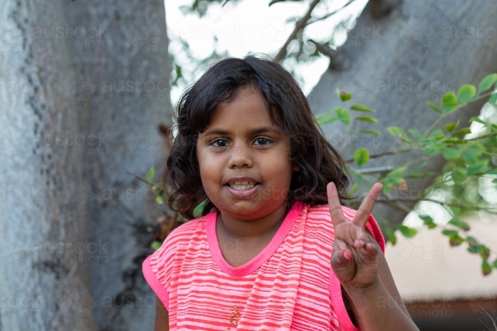 little girl sitting in tree making finger signs - Australian Stock Image