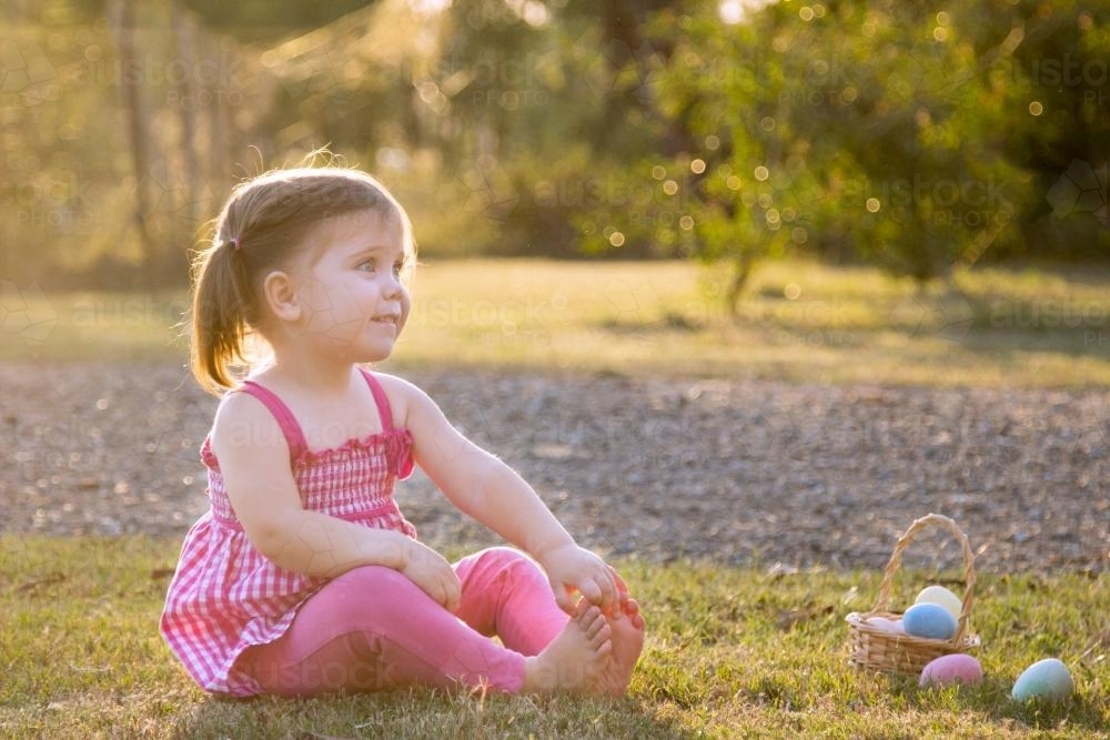 Little girl sitting next to a basket of Easter eggs - Australian Stock Image