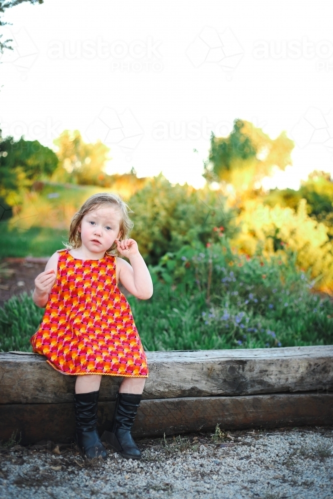 Little girl sitting on log in lush garden setting - Australian Stock Image