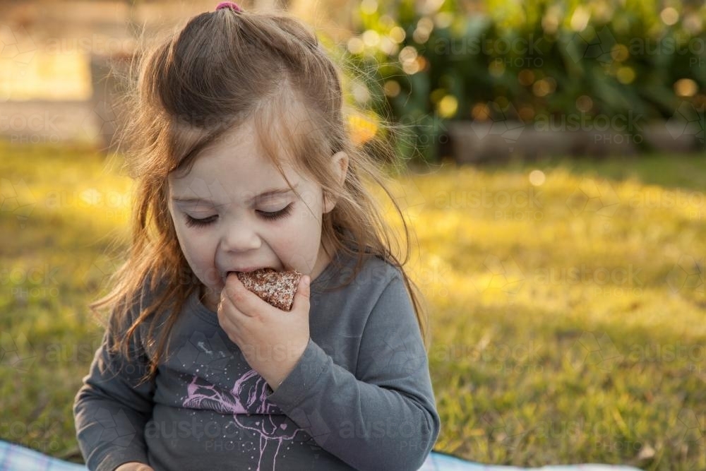 Little girl sitting outside eating a lamington - Australian Stock Image