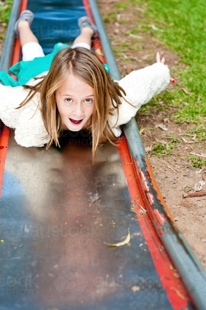 Little girl sliding down a slippery slide on her tummy - Australian Stock Image