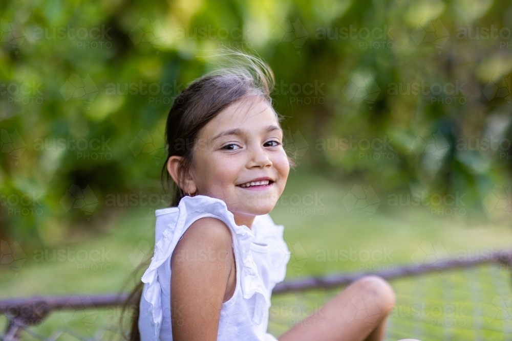 little girl smiling looking at camera over shoulder - Australian Stock Image