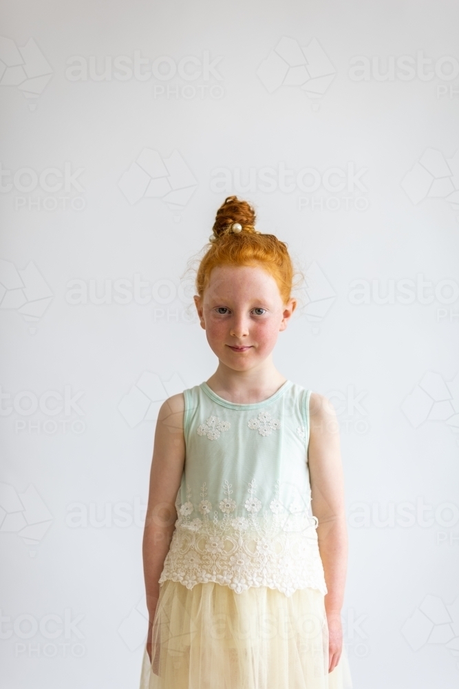 little girl standing straight looking at camera against plain background - Australian Stock Image