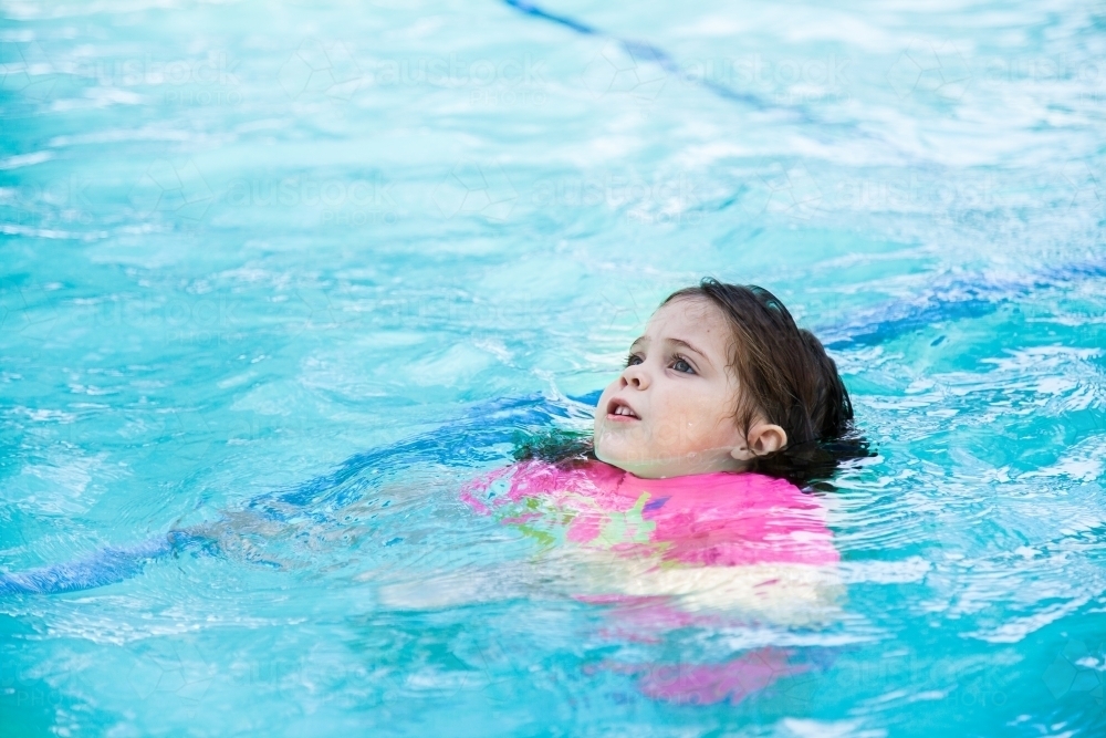 Little girl swimming in backyard pool looking worried - Australian Stock Image