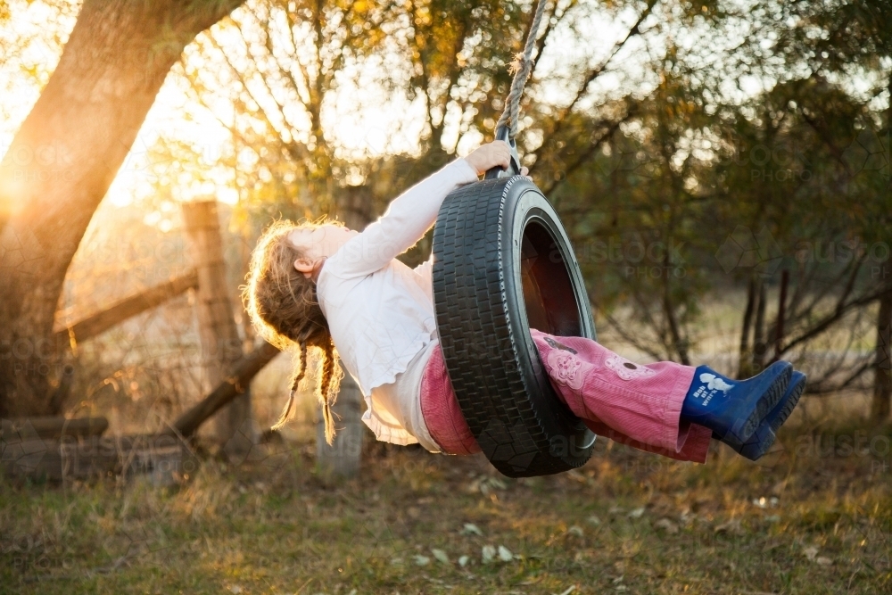 Little girl swinging on tire swing with sun flare - Australian Stock Image