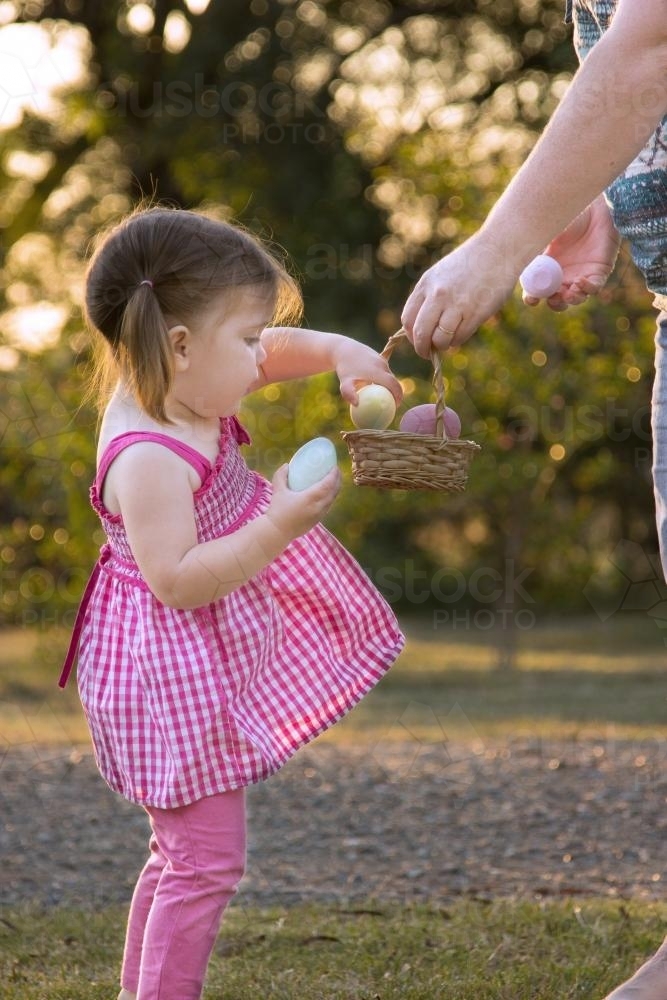 Little girl taking Easter eggs from the basket her mother is holding - Australian Stock Image