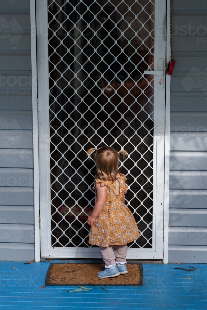 Little girl toddler standing at front door of home - Australian Stock Image