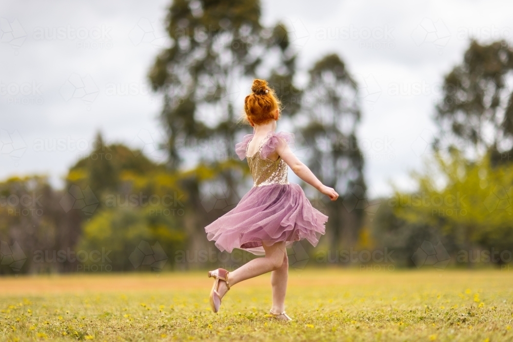 little girl twirling in pretty dress outdoors - Australian Stock Image