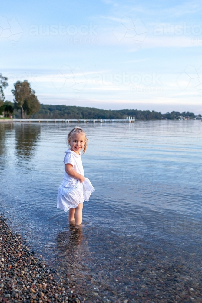 Little girl wading in water of coastal lake at sunset - Australian Stock Image