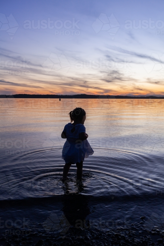 Little girl wading in water of coastal lake at sunset - Australian Stock Image