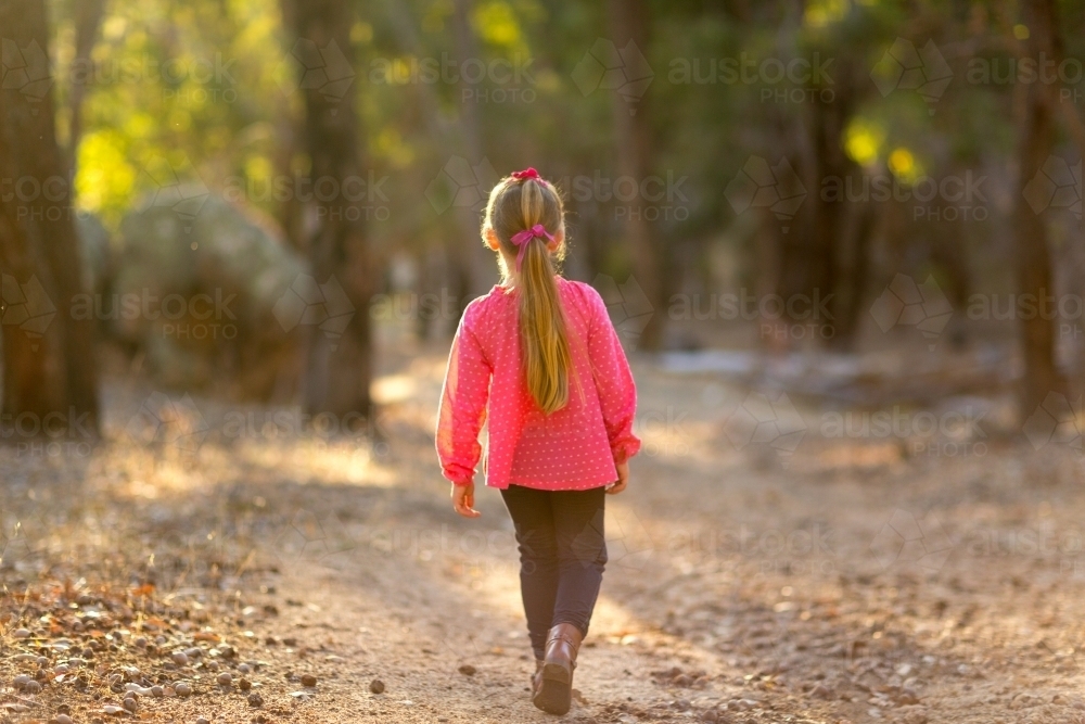 Little girl walking away into golden light in bushland - Australian Stock Image