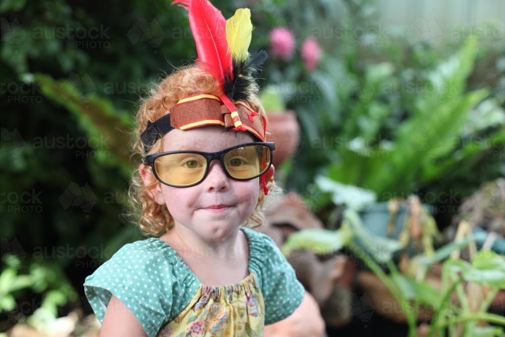 Little girl wearing dress up Indian headband and glasses - Australian Stock Image