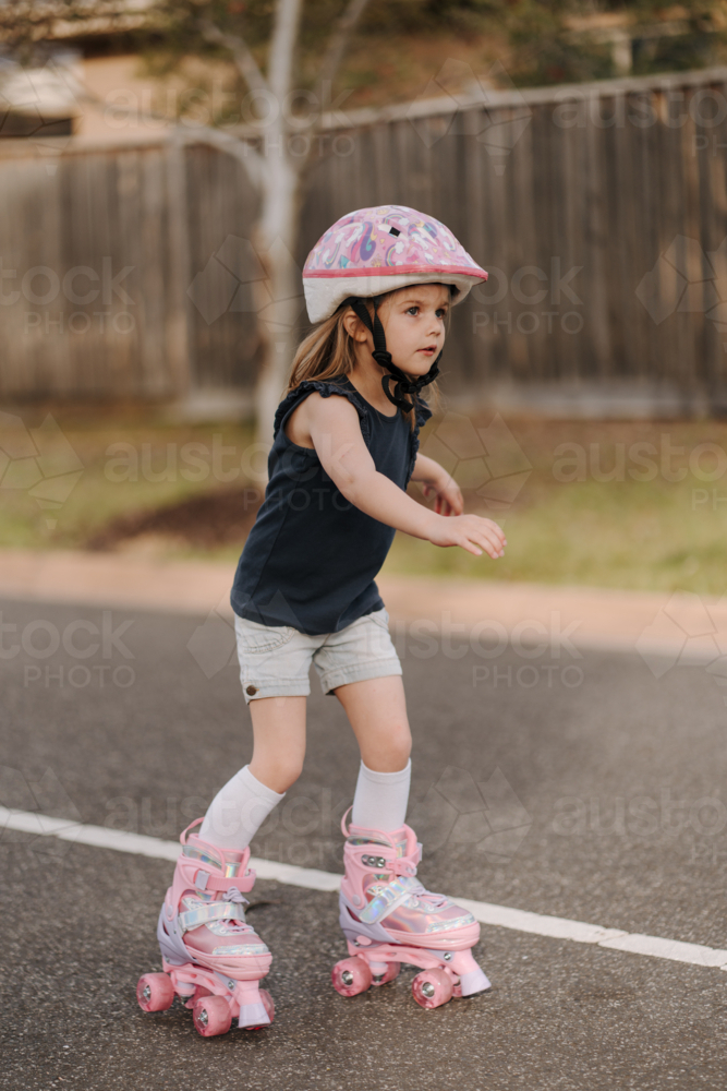 Little girl wearing pink helmet on four-wheeled roller skates - Australian Stock Image