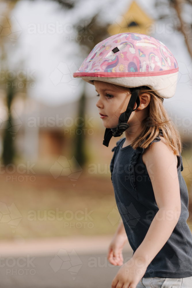 Little girl wearing pink helmet playing outside - Australian Stock Image