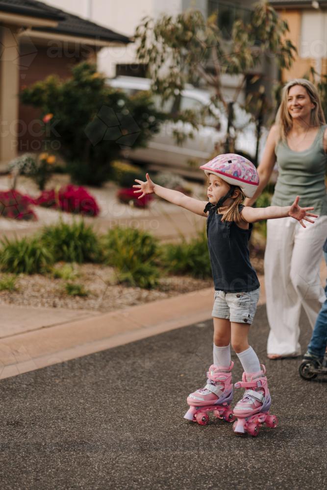Little girl wearing pink helmet while on roller skates spreads her arms wide open. - Australian Stock Image