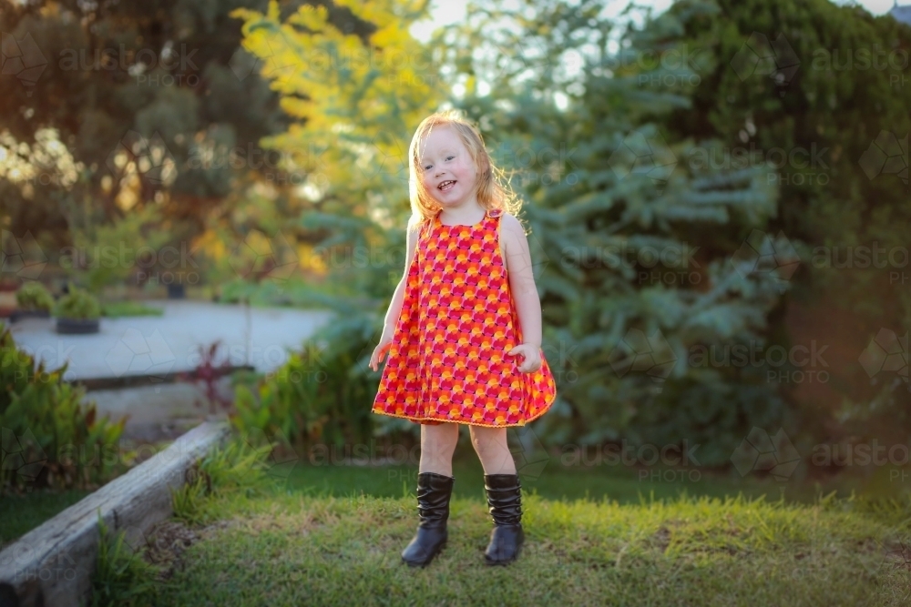 Little girl wearing red dress exploring lush green garden - Australian Stock Image