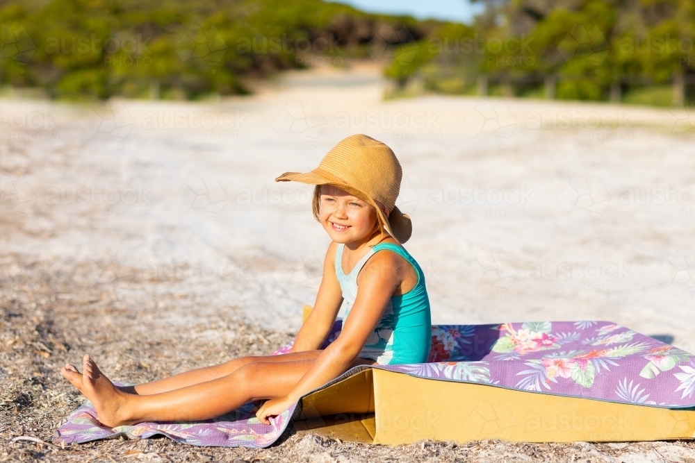 Little girl wearing straw hat sitting on sand - Australian Stock Image