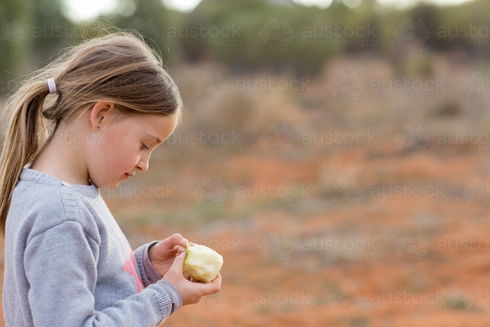 Little girl with apple outside with red dirt - Australian Stock Image