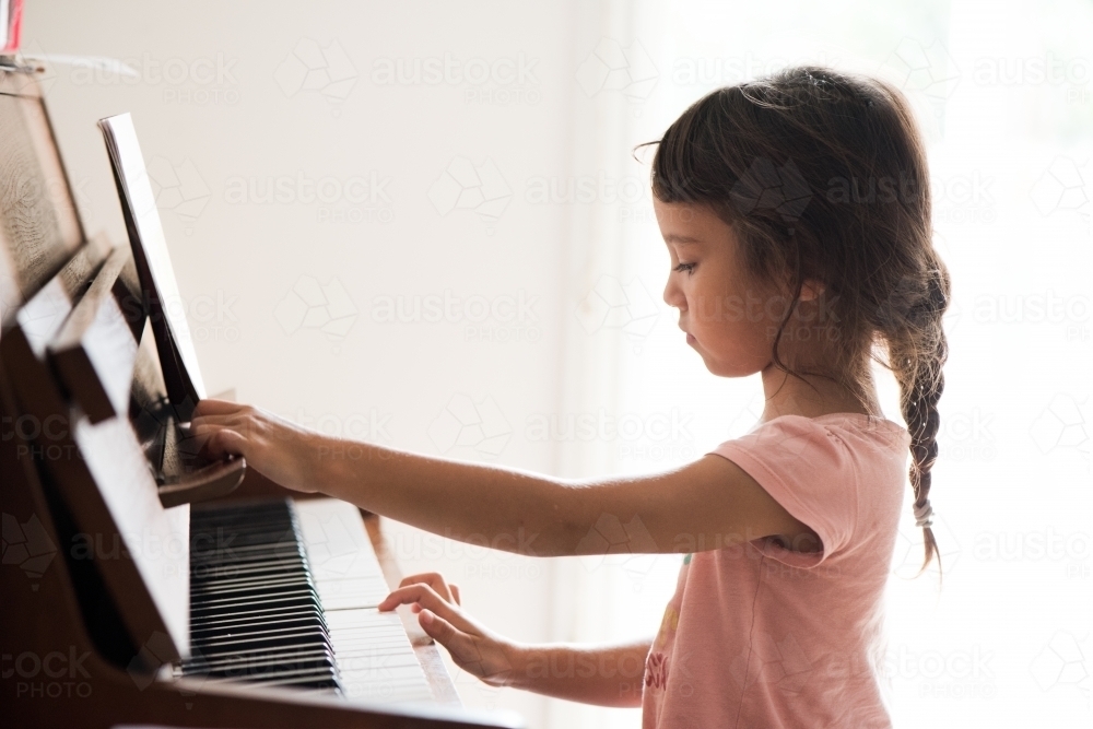 Little girl with Asian ethnicity learning to play the piano. - Australian Stock Image