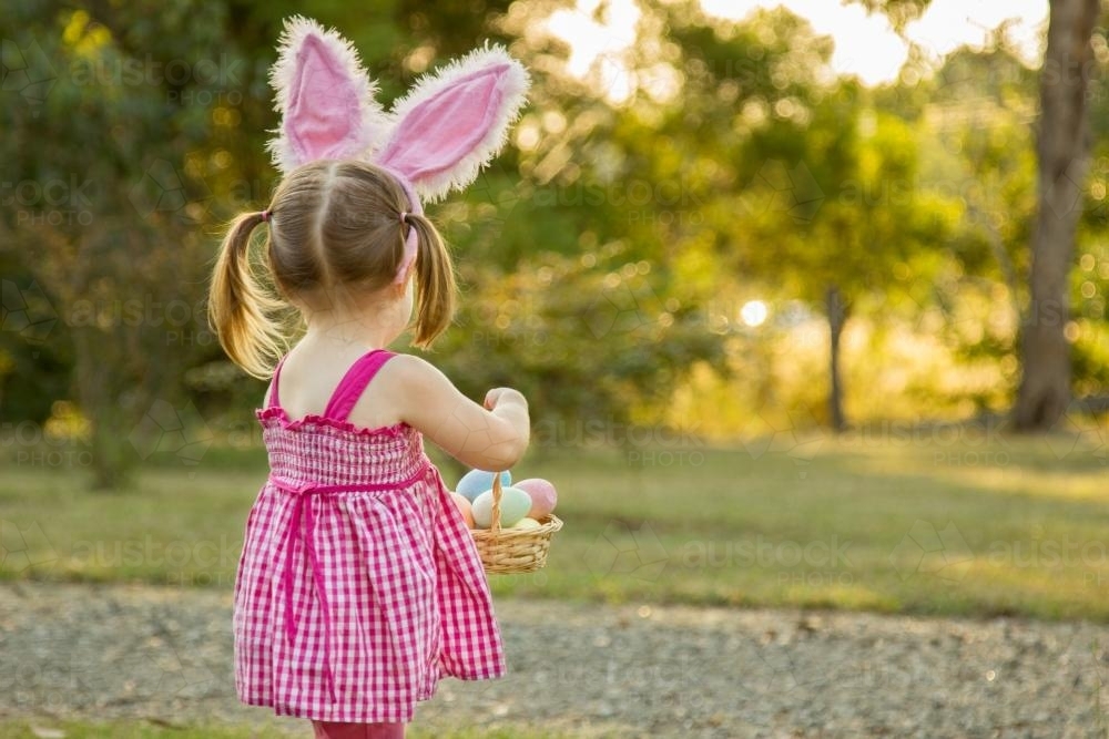 Little girl with bunny ears carrying a basket of Easter eggs - Australian Stock Image
