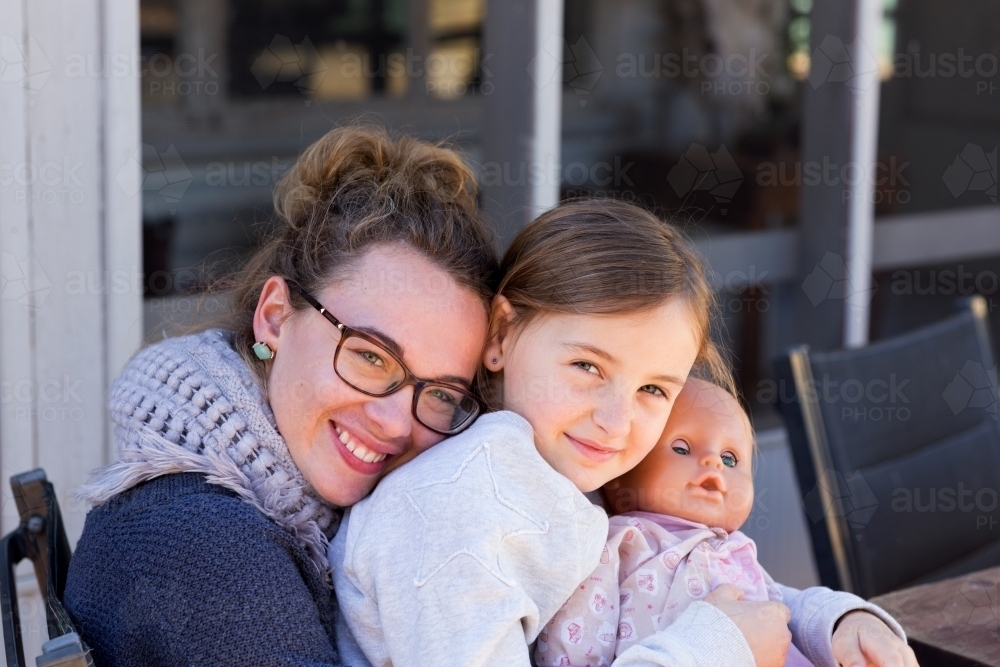 Little girl with dolly sitting on the lap of her governess - Australian Stock Image