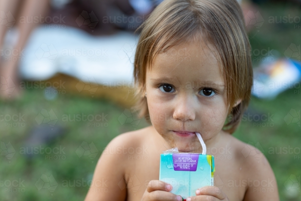 little girl with grubby face drinking from juice box - Australian Stock Image