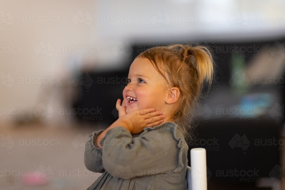 little girl with hands under chin smiling and looking out of frame - Australian Stock Image