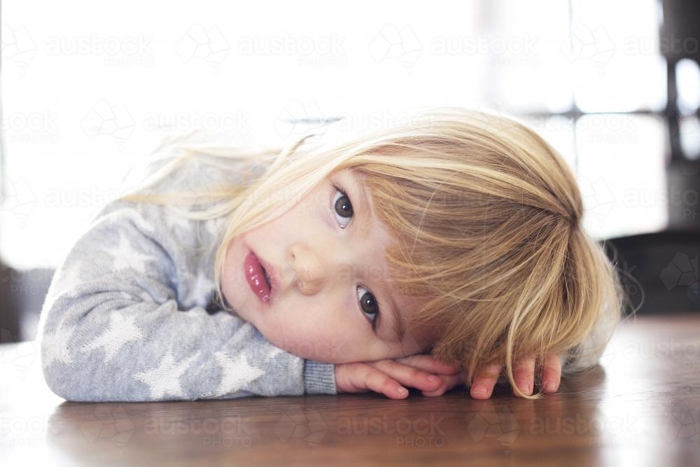 Little girl with head and hands on a table - Australian Stock Image
