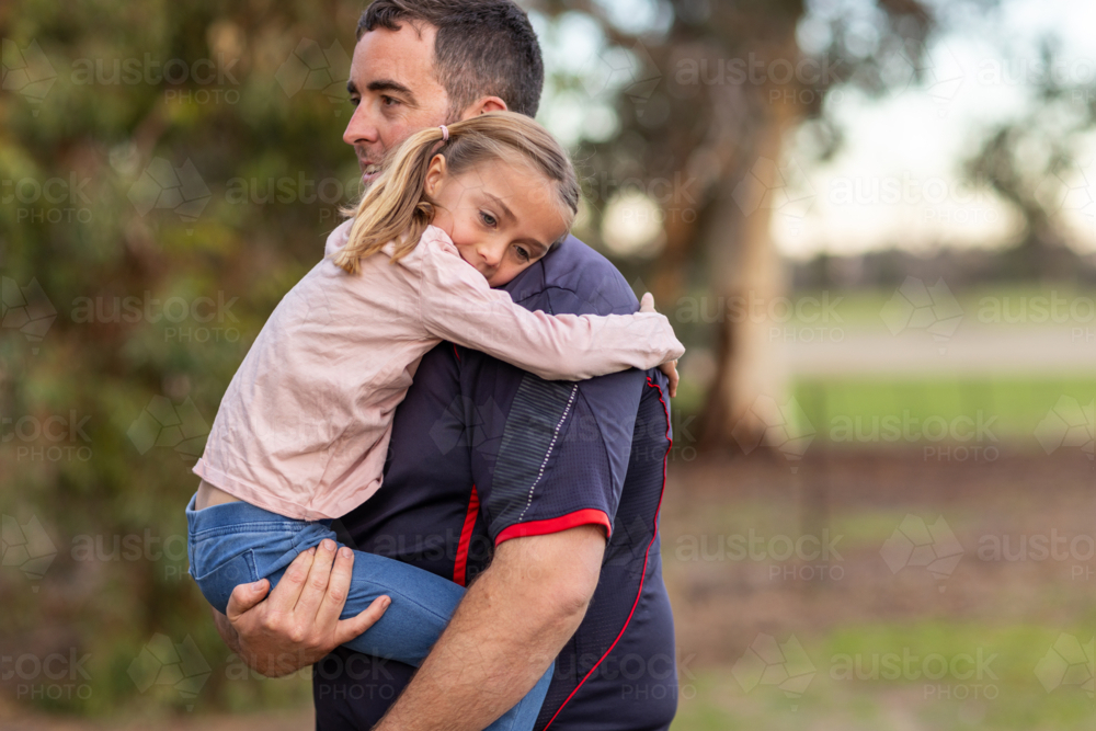 little girl with her arms around her father's neck as he carries her - Australian Stock Image