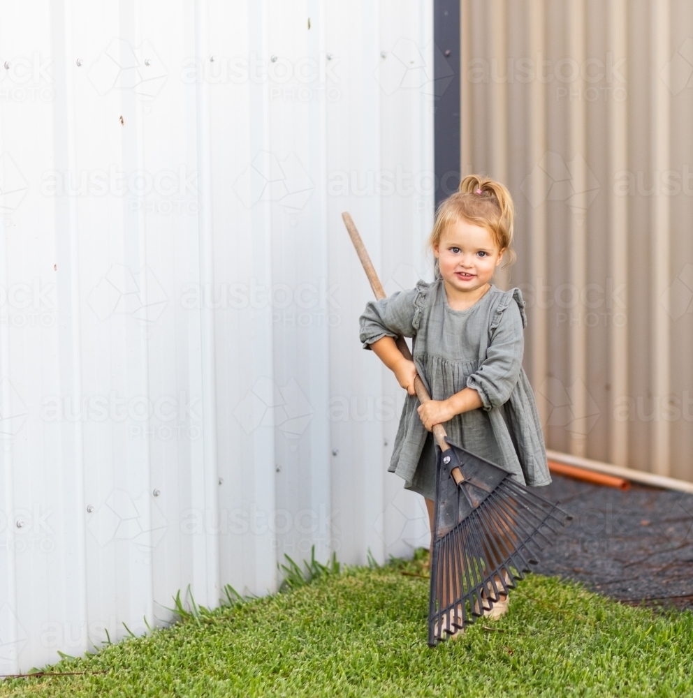 Image of little girl with lawn rake in backyard - Austockphoto