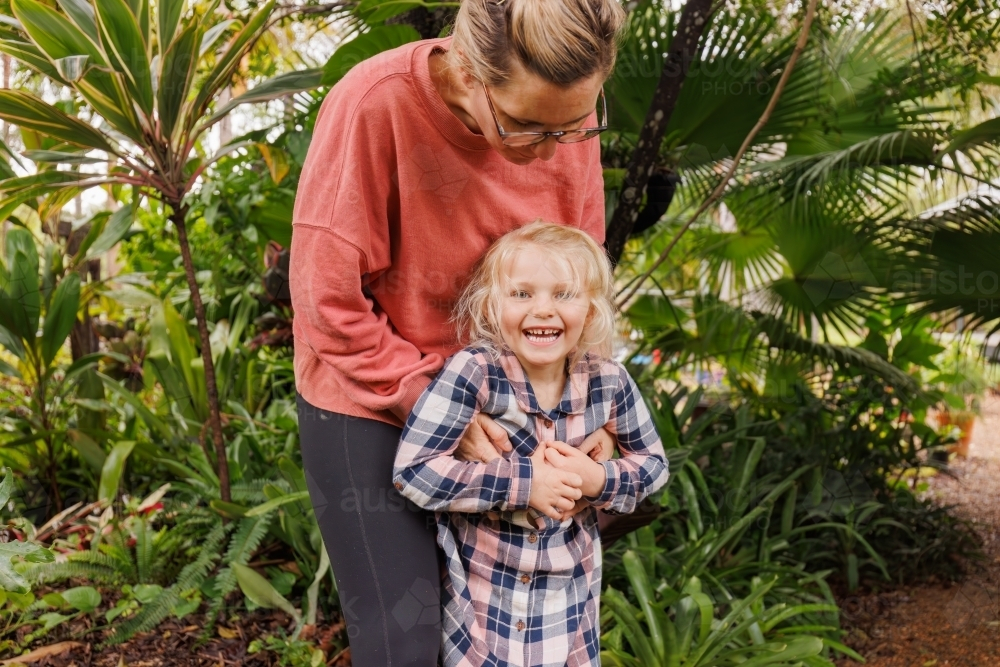 Little girl with messy hair smiling while getting tickled by mother - Australian Stock Image