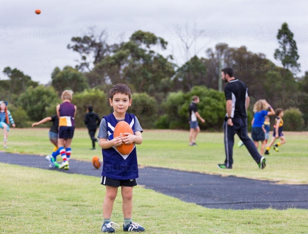 Little kid holding football at Auskick footy - Australian Stock Image