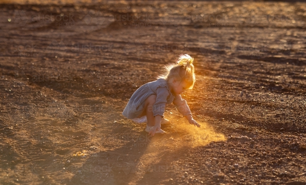 little kid playing in the dirt with backlight highlighting dust - Australian Stock Image