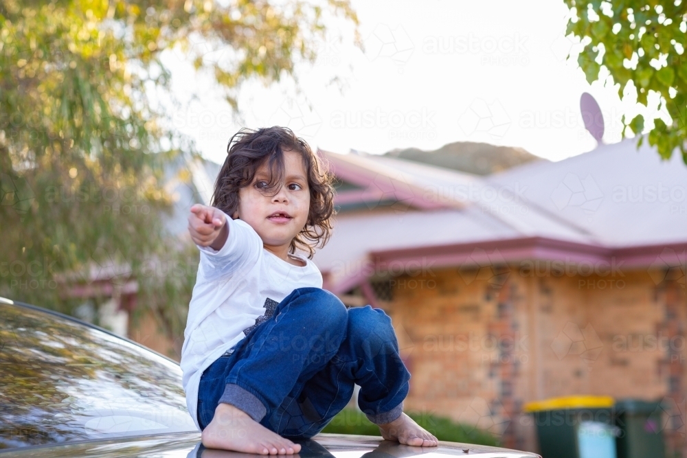 Little kid sitting on car boot pointing - Australian Stock Image