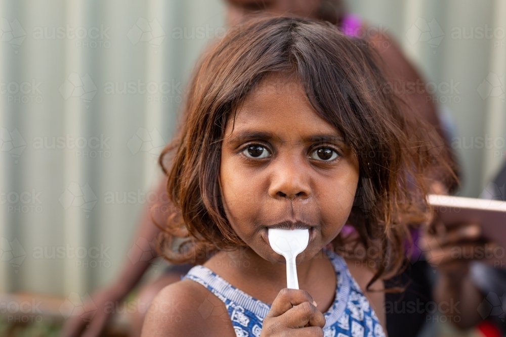 little kid with plastic spoon in mouth looking at camera - Australian Stock Image