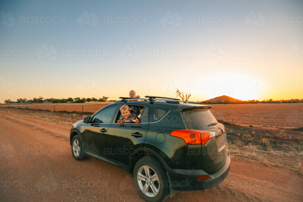 Little kids hanging out window and sunroof of small vehicle on dirt road - Australian Stock Image