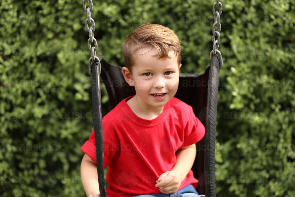 Little preschool age boy playing on backyard tyre swing - Australian Stock Image