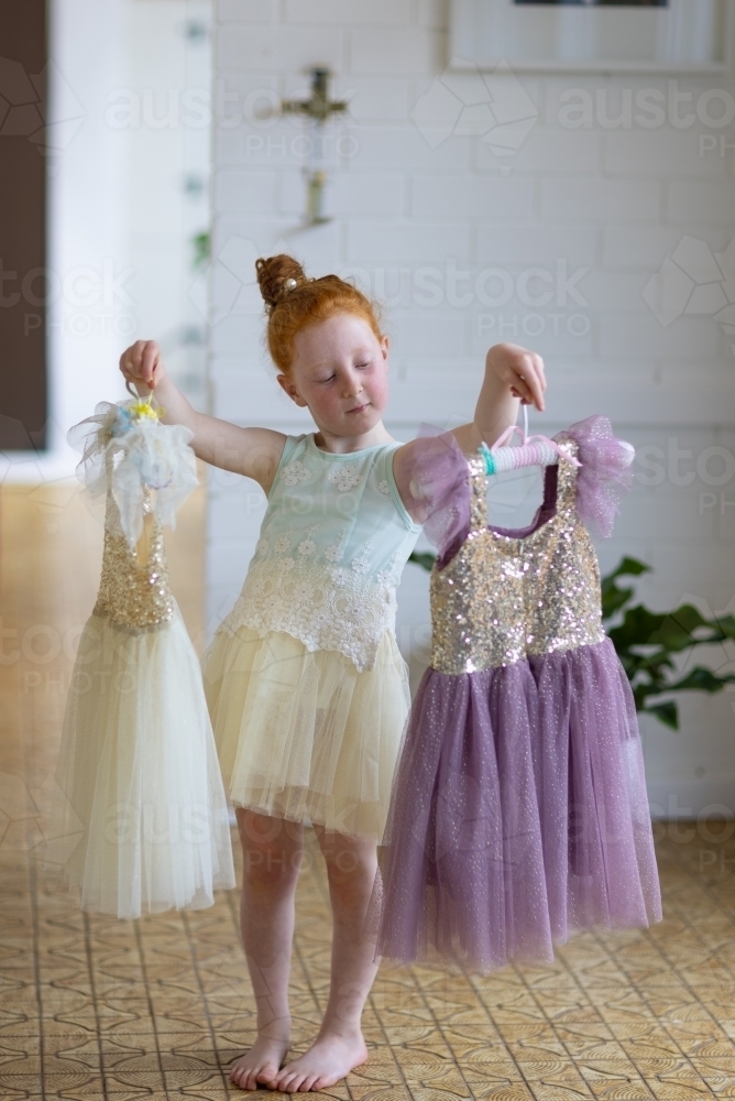 little red-haired girl choosing which pretty dress to wear - Australian Stock Image