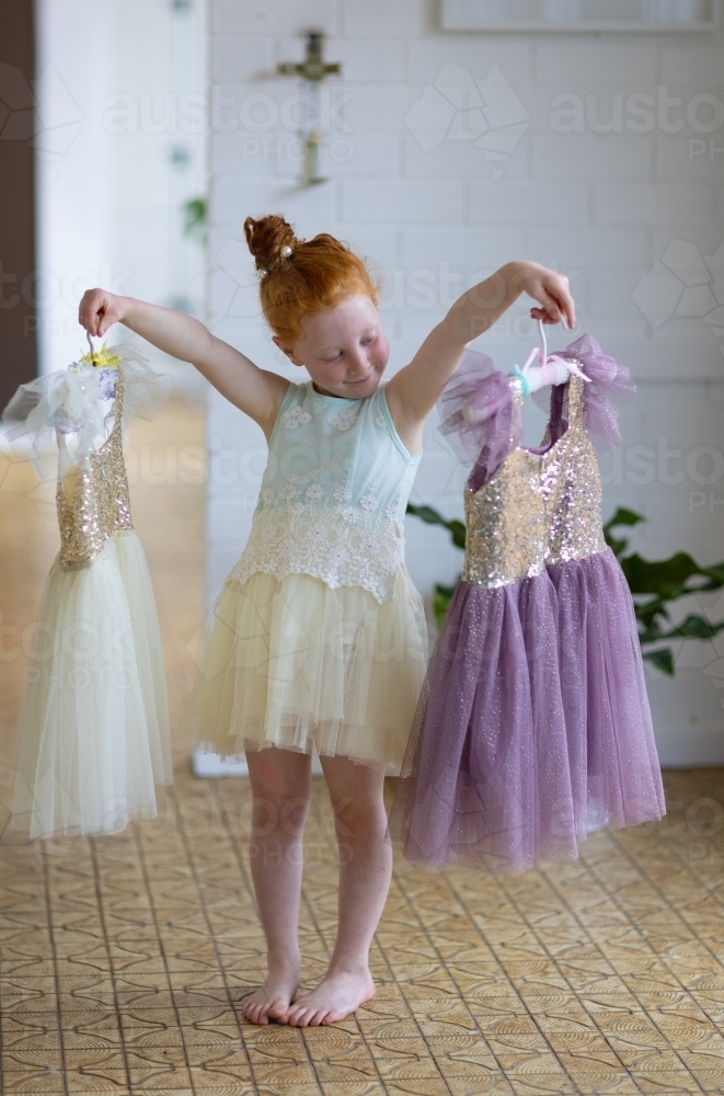 little red-haired girl choosing which pretty dress to wear - Australian Stock Image