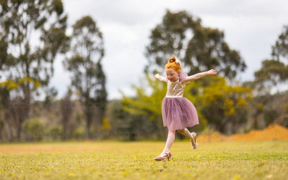 little red-headed girl leaping outdoors wearing pretty sequinned dress - Australian Stock Image